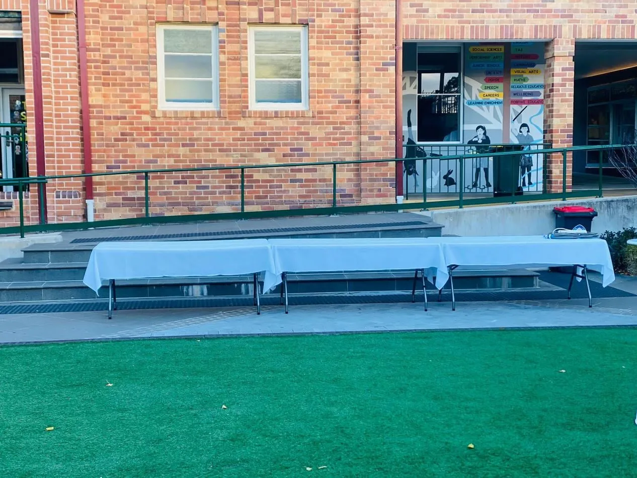 A plastic trestle table set up on a grassy area in front of a building.