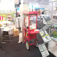 A man standing next to a popcorn cart at a trade show.