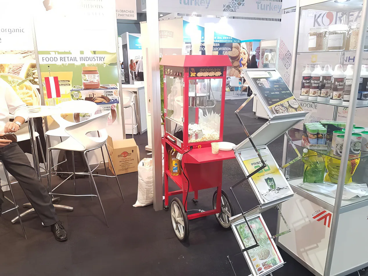A man standing next to a popcorn cart at a trade show.