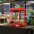 Close-up of a red commercial popcorn machine on a table in an indoor venue with plants and ambient lighting in the background