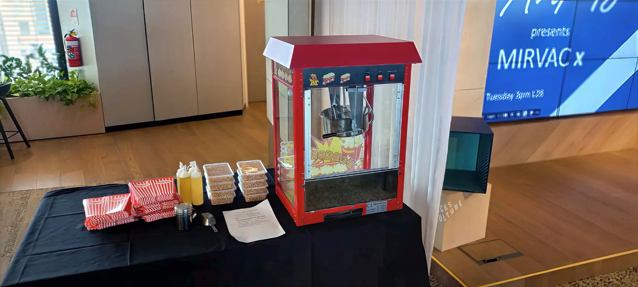 Popcorn machine set up on a serving table with popcorn boxes, oil bottles, and kernels ready for use at an indoor event