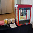 Popcorn machine set up on a serving table with popcorn boxes, oil bottles, and kernels ready for use at an indoor event