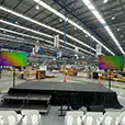 Portable event stage setup inside a large warehouse with dual presentation screens, speakers, stairs access, and rows of audience seating