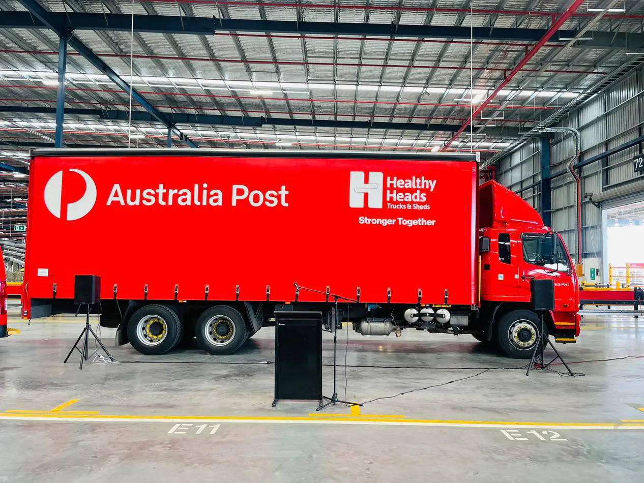 Portable PA system with speakers on stands and microphone setup positioned in front of Australia Post truck inside large warehouse event space