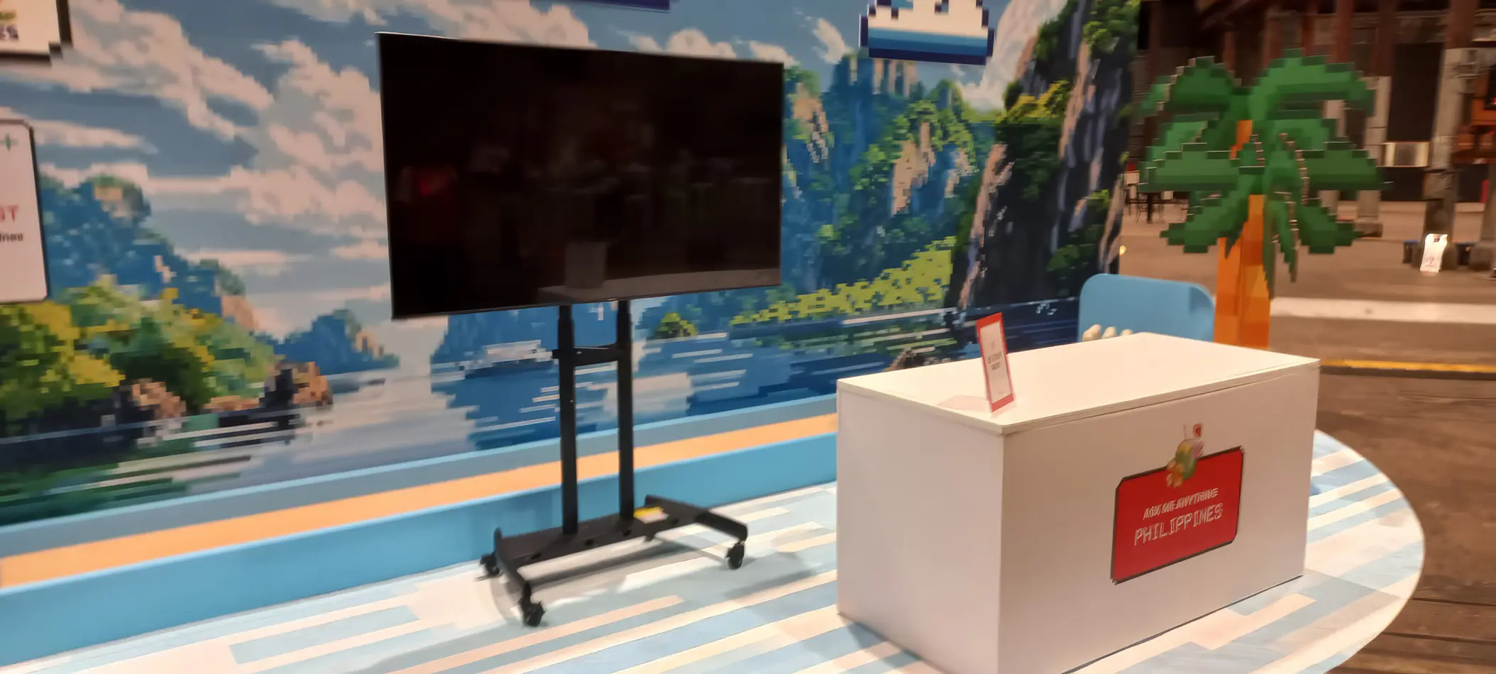 Portable TV display mounted on a wheeled stand positioned at an indoor exhibition booth with branded counter and themed backdrop