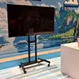 Portable TV display mounted on a wheeled stand positioned at an indoor exhibition booth with branded counter and themed backdrop