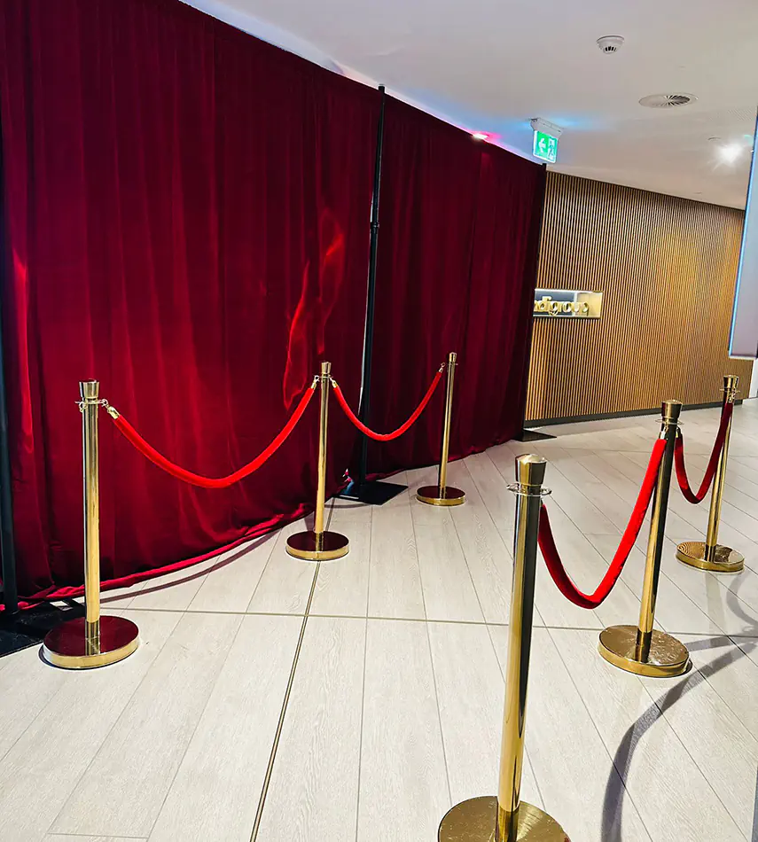 Red velvet event backdrop with gold barrier posts and rope dividers creating a VIP-style entrance display