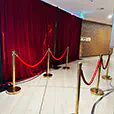 Red velvet event backdrop with gold barrier posts and rope dividers creating a VIP-style entrance display