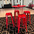 Red wire cocktail table with matching bar stools positioned in an indoor event space with patterned carpet flooring