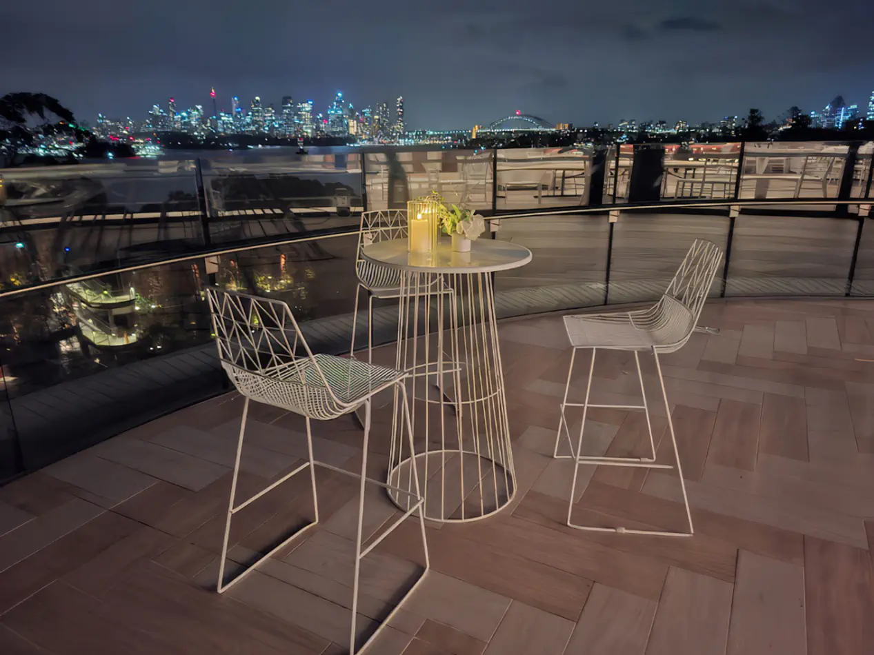White wire cocktail table with matching stools on a rooftop terrace at night overlooking city skyline, styled with candles and decorative elements