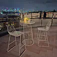White wire cocktail table with matching stools on a rooftop terrace at night overlooking city skyline, styled with candles and decorative elements