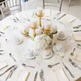 A round plastic banquet table with a white and gold table setting for a wedding reception.
