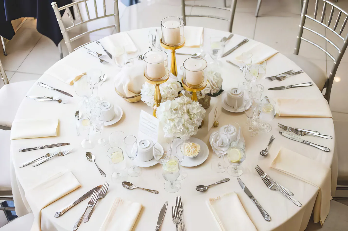 A round plastic banquet table with a white and gold table setting for a wedding reception.
