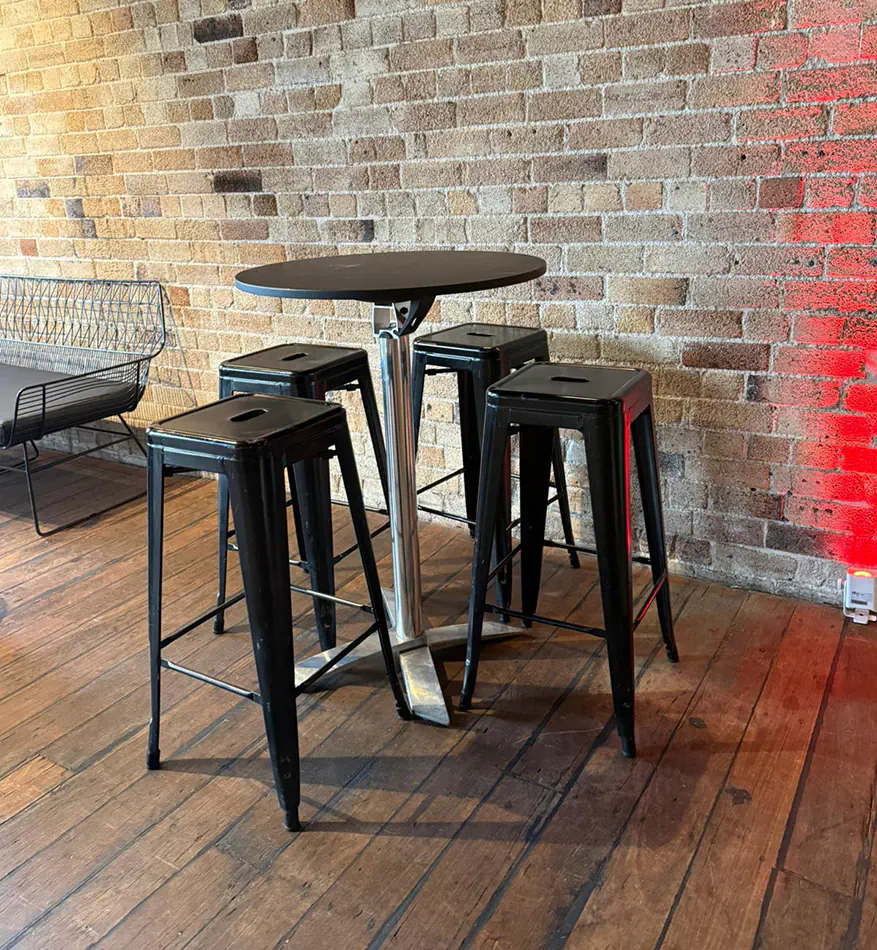 Round black cocktail table surrounded by industrial black bar stools inside a rustic event venue with timber flooring