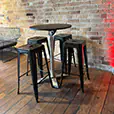 Round black cocktail table surrounded by industrial black bar stools inside a rustic event venue with timber flooring