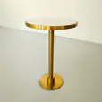 Modern round gold cocktail table with a sleek pedestal base and white tabletop, styled against a neutral background.