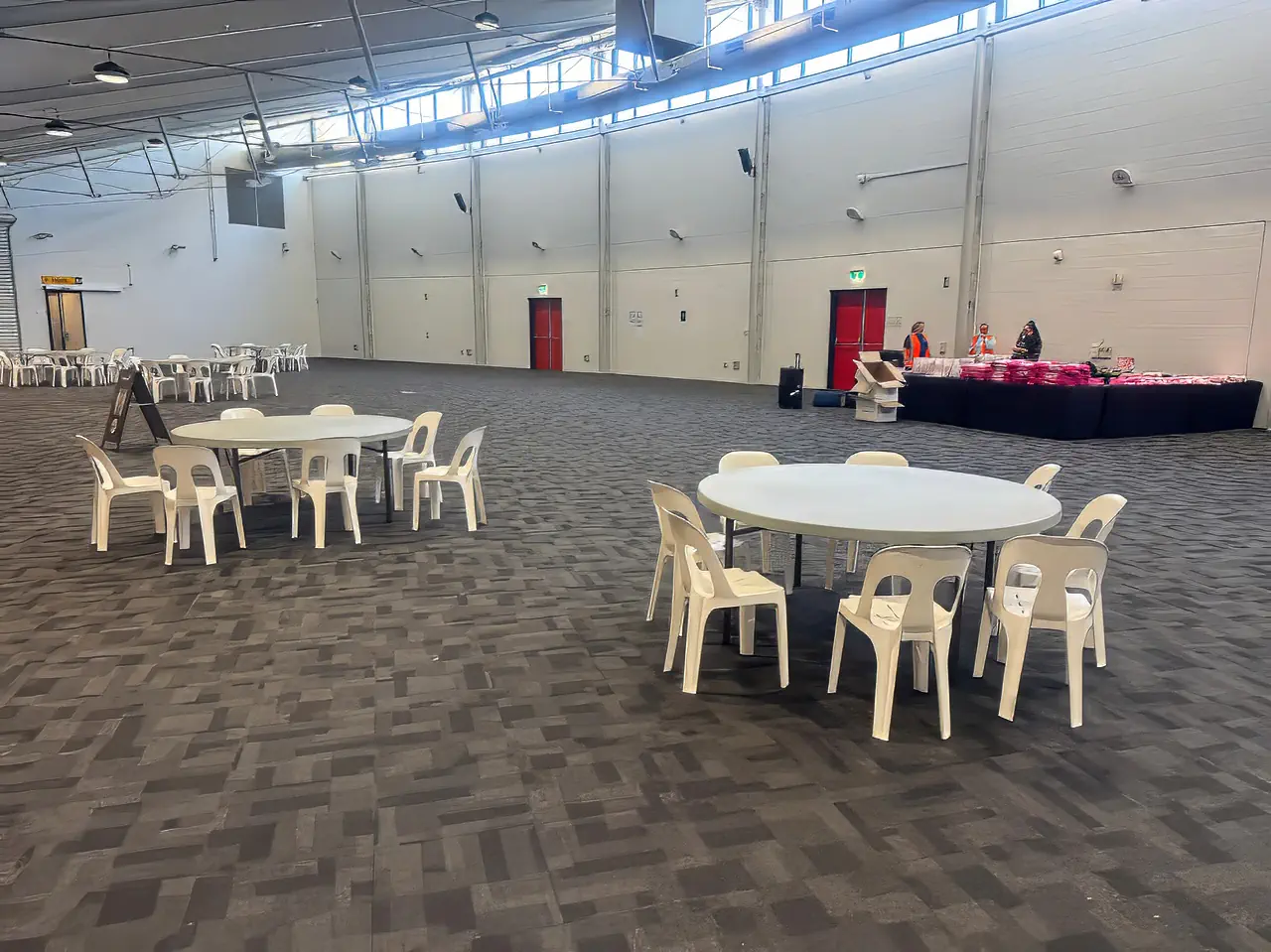 Spacious indoor community venue with round plastic banquet tables and casual seating arranged across an open hall