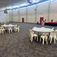 Spacious indoor community venue with round plastic banquet tables and casual seating arranged across an open hall