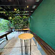 Round timber top cocktail tables with black hairpin legs arranged in a covered outdoor space with greenery, bench seating and hanging lights