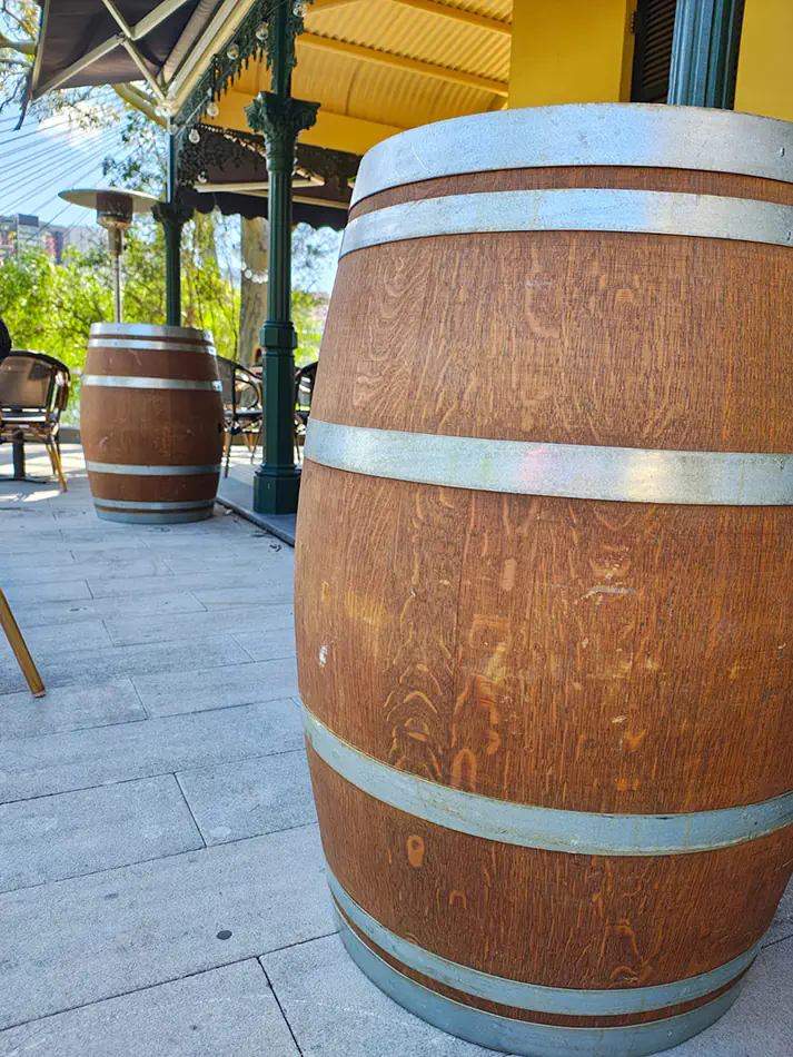Rustic wooden wine barrel cocktail tables placed in an outdoor venue seating area with covered veranda and surrounding furniture