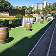 Rustic timber wine barrels arranged along a racecourse event walkway with artificial turf and outdoor entertainment area