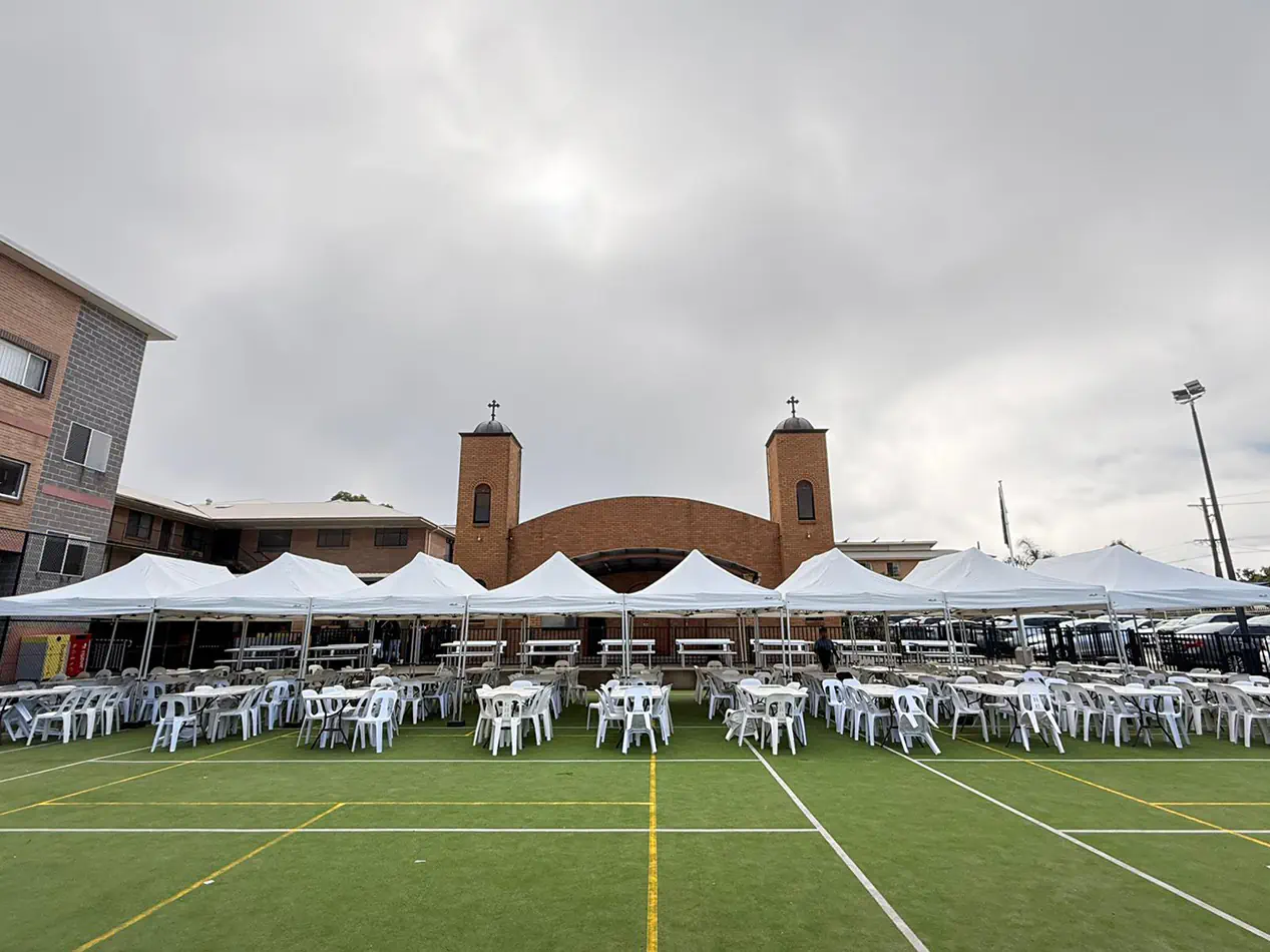 Long row of white pop-up marquees with outdoor dining tables and chairs arranged for a school or community event