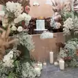 A wedding cake decorated with flowers, candles, and a clear square acrylic plinth.