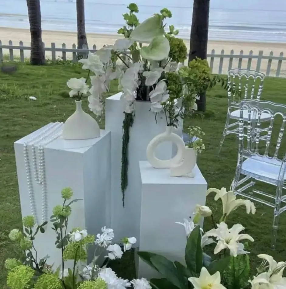 A white flower arrangement on a table in front of a beach, displayed on white square plinths.