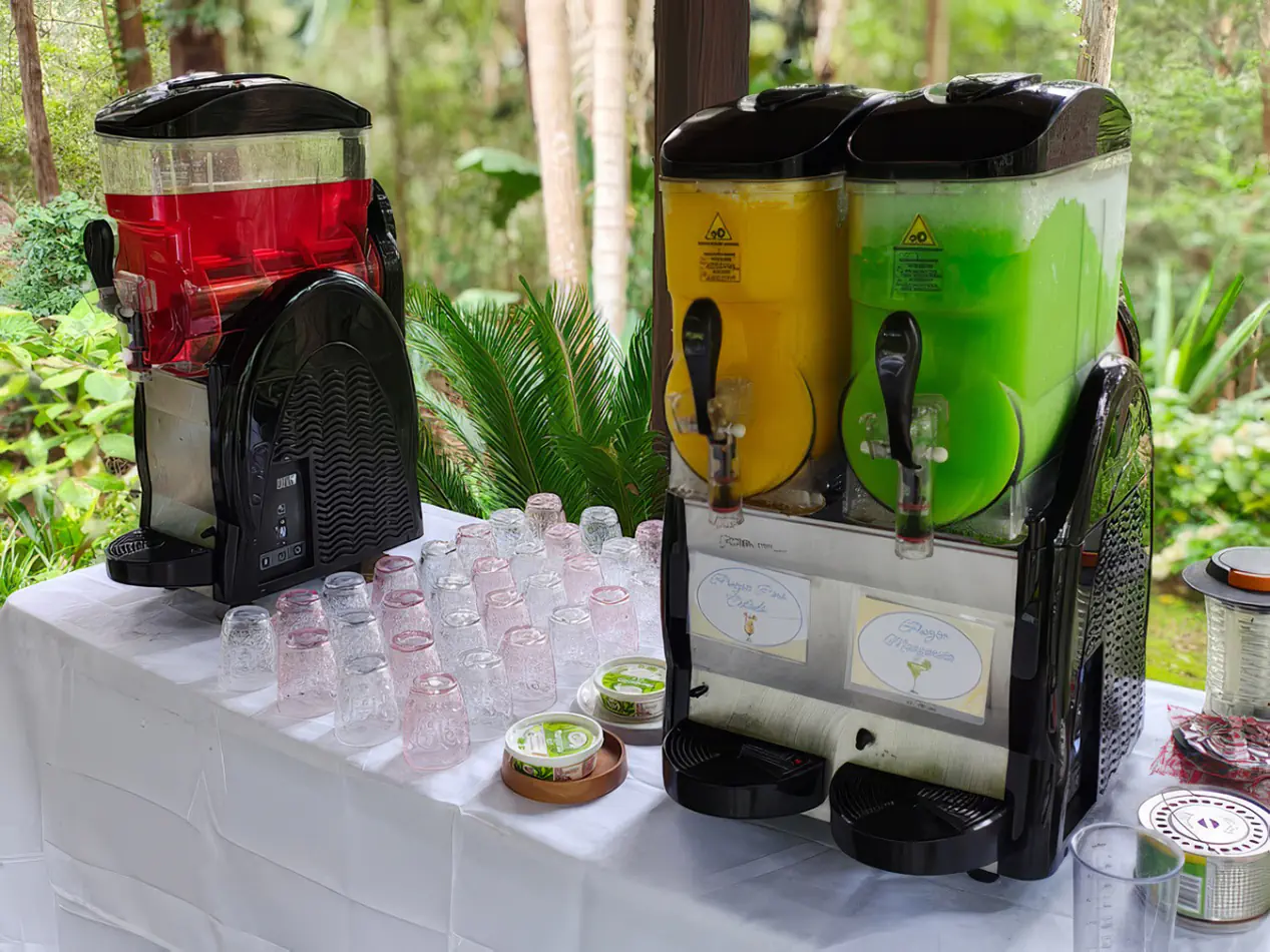 Slushie machine hire with multiple flavour dispensers in red, yellow and green set up on a table with cups for outdoor event service