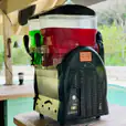 A slushie machine sitting on a table next to a pool, offering 120 refreshing drinks.