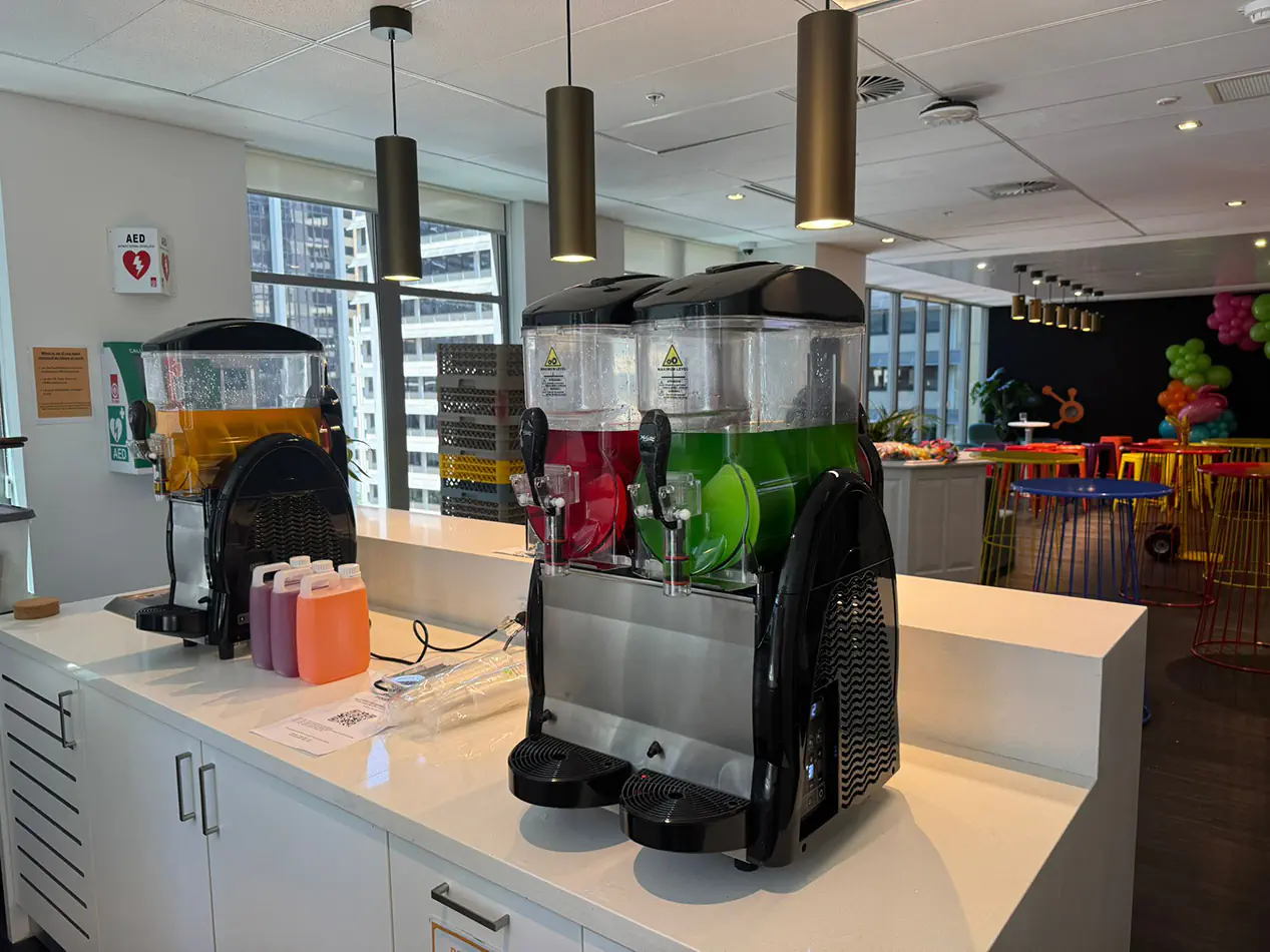 Slushie machines on a counter with colourful drink dispensers filled with frozen beverages in an indoor event setting