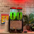 A soda machine with two green drinks on it, available for Slushie Machine Hire: Pkg 3 - *240 Drinks*.