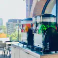 Two slushie machines on a balcony with a view of the city, offering *240 drinks* in total.