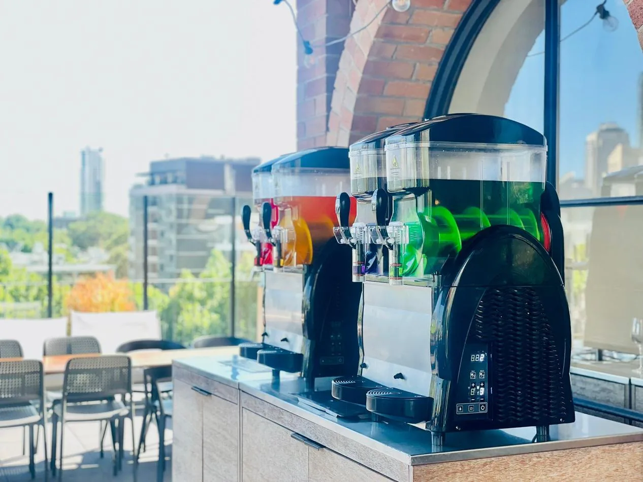 Two slushie machines on a balcony with a view of the city, offering *240 drinks* in total.