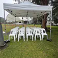 Small white pop-up marquee with rows of white event chairs set up in a public park for an outdoor gathering