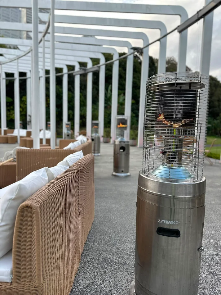 Stainless steel outdoor area heater providing warmth beside lounge seating on a covered event terrace