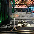Stainless steel cocktail table positioned inside a modern event venue with patterned carpet, exposed ceiling beams, and ambient coloured lighting
