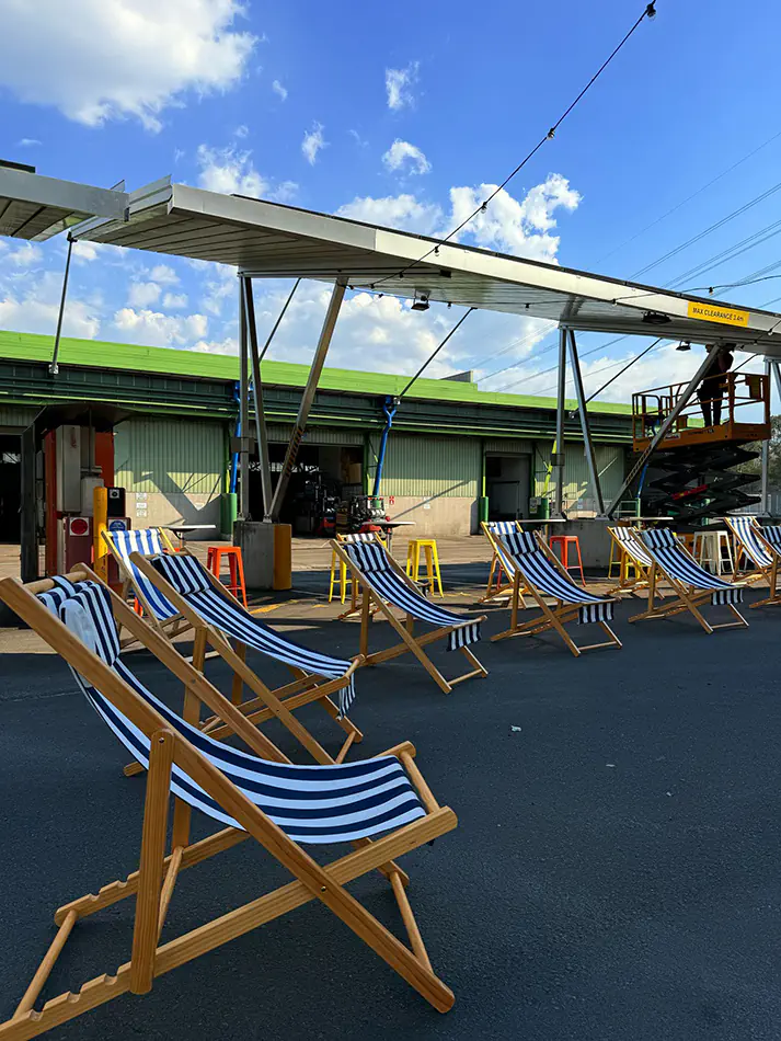 Blue and white striped deck chairs arranged in a row at an outdoor event space with open sky, industrial structure and casual seating setup