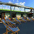 Blue and white striped deck chairs arranged in a row at an outdoor event space with open sky, industrial structure and casual seating setup