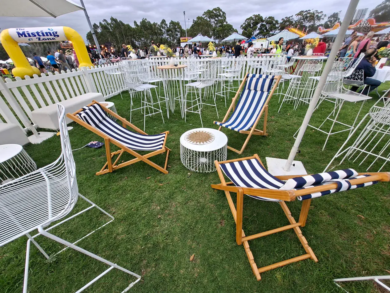 Blue and white striped deck chairs arranged in an outdoor festival lounge area with white wire furniture and casual seating