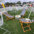 Blue and white striped deck chairs arranged in an outdoor festival lounge area with white wire furniture and casual seating
