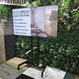 TV hire display screen on a stand inside an exhibition booth with acoustic wall panels, greenery backdrop and branded signage for a trade show display
