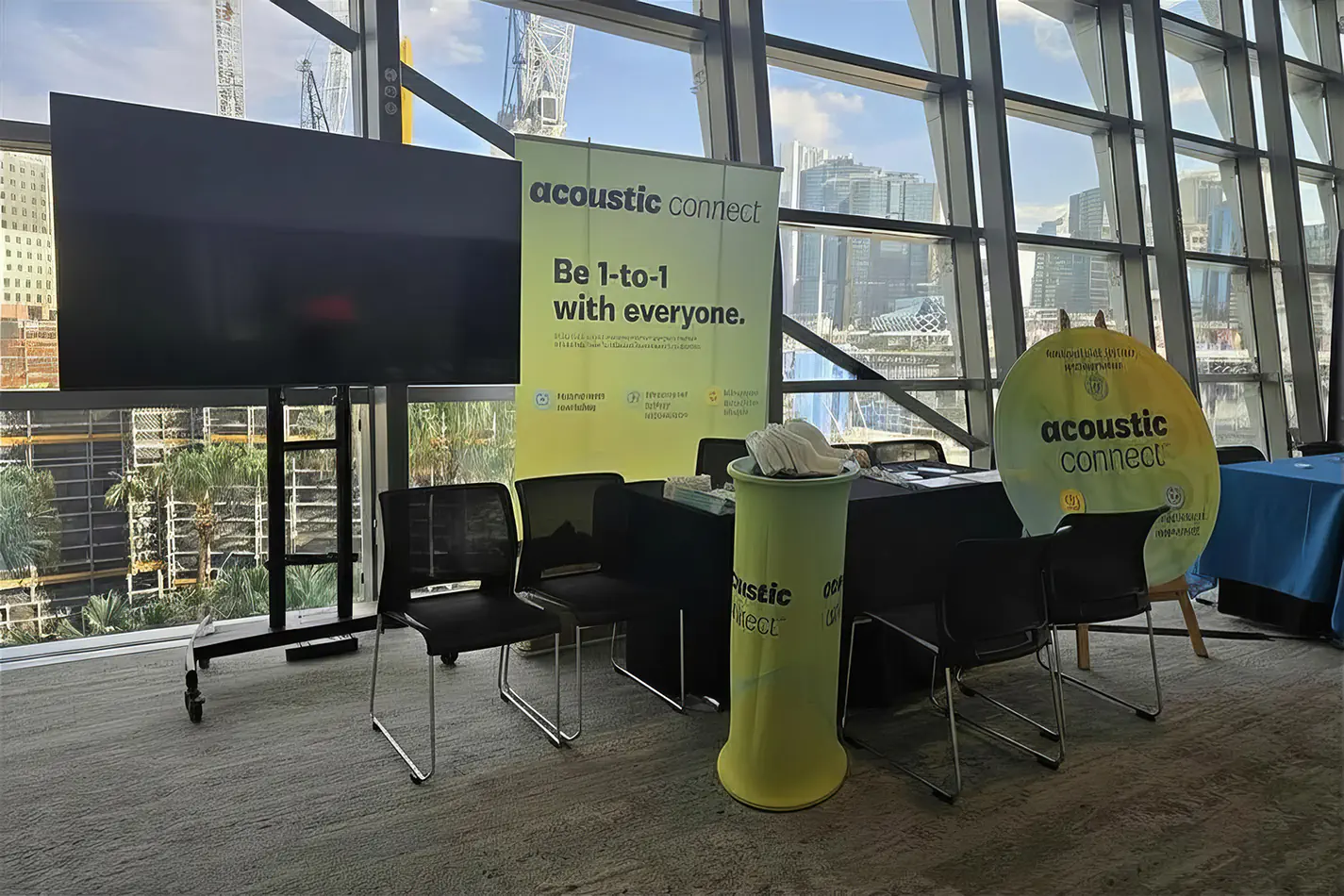 TV hire setup for a corporate trade show display with branded signage, seating, event table and city views through large glass windows