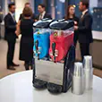 Twin bowl frozen drink machine with blue and red beverages displayed at a corporate event with serving cups nearby