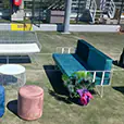 Outdoor lounge seating setup with green and pink velvet sofas, matching ottomans and a round coffee table arranged on artificial grass