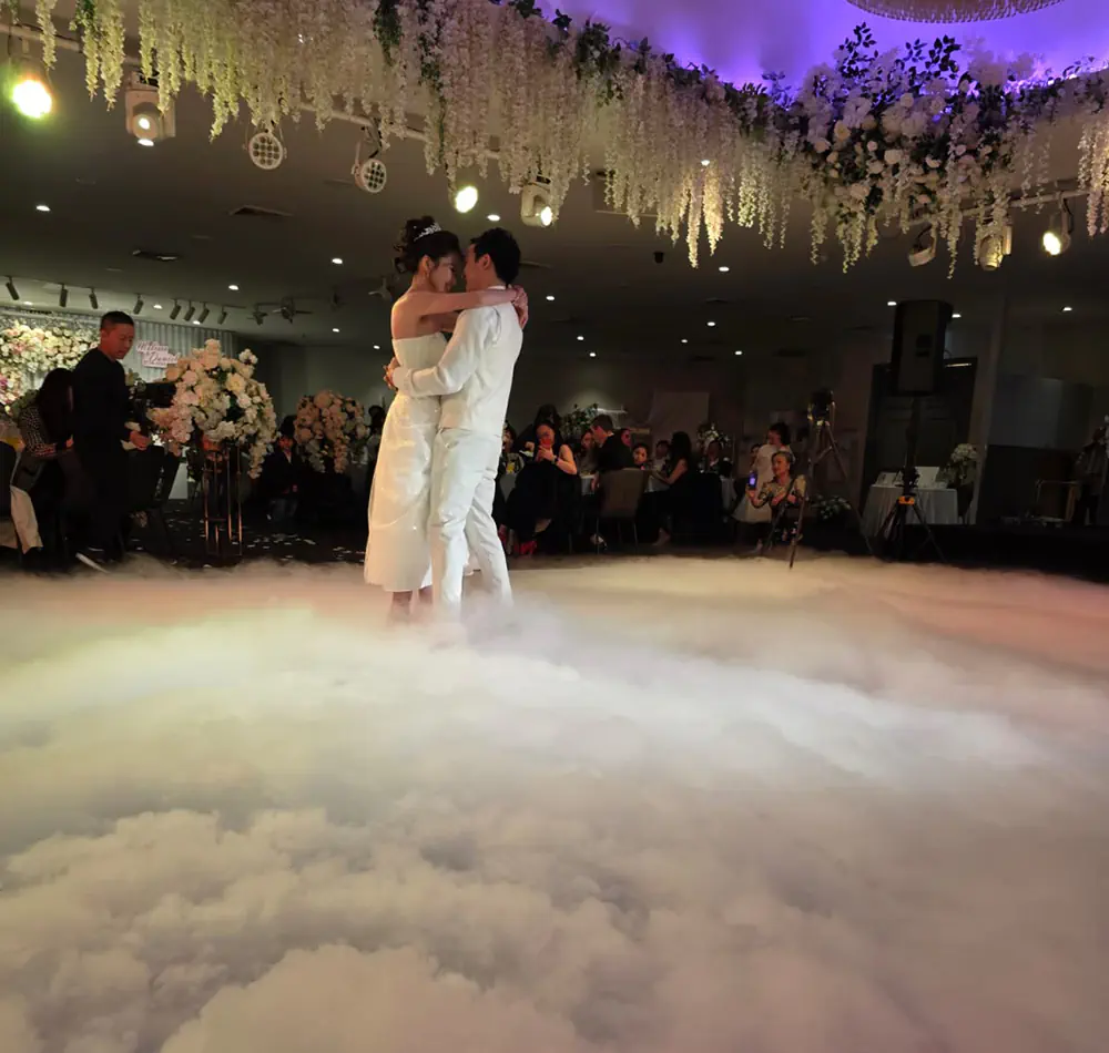 Bride and groom dancing on a low-lying dry ice cloud effect during a wedding reception with floral ceiling installations