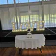 Wedding stage with white draping, illuminated LOVE letters and a cake table set in front on polished timber flooring