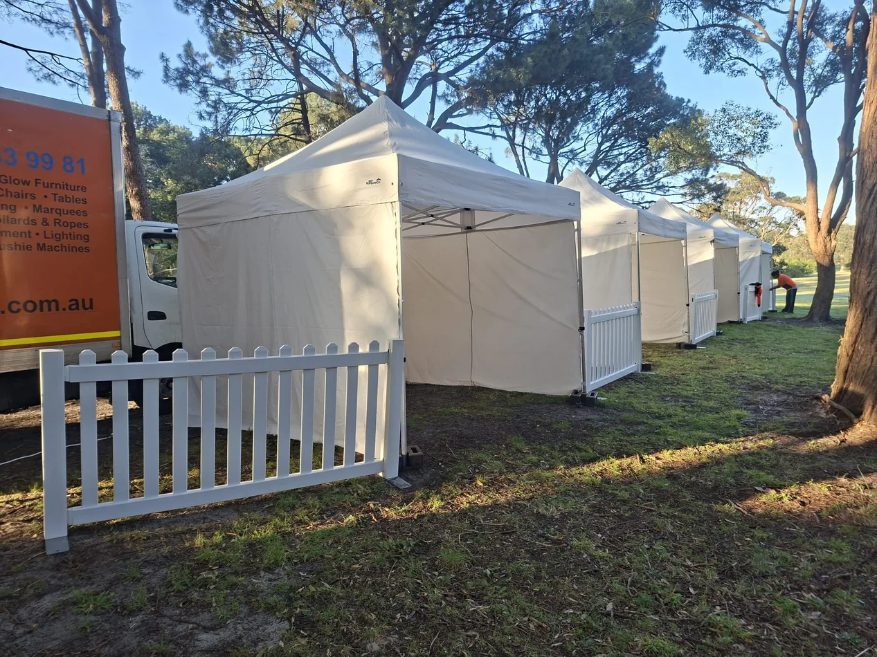 White 3x3m pop-up marquees with three-sided walls arranged as sheltered event booths on a grassed park site