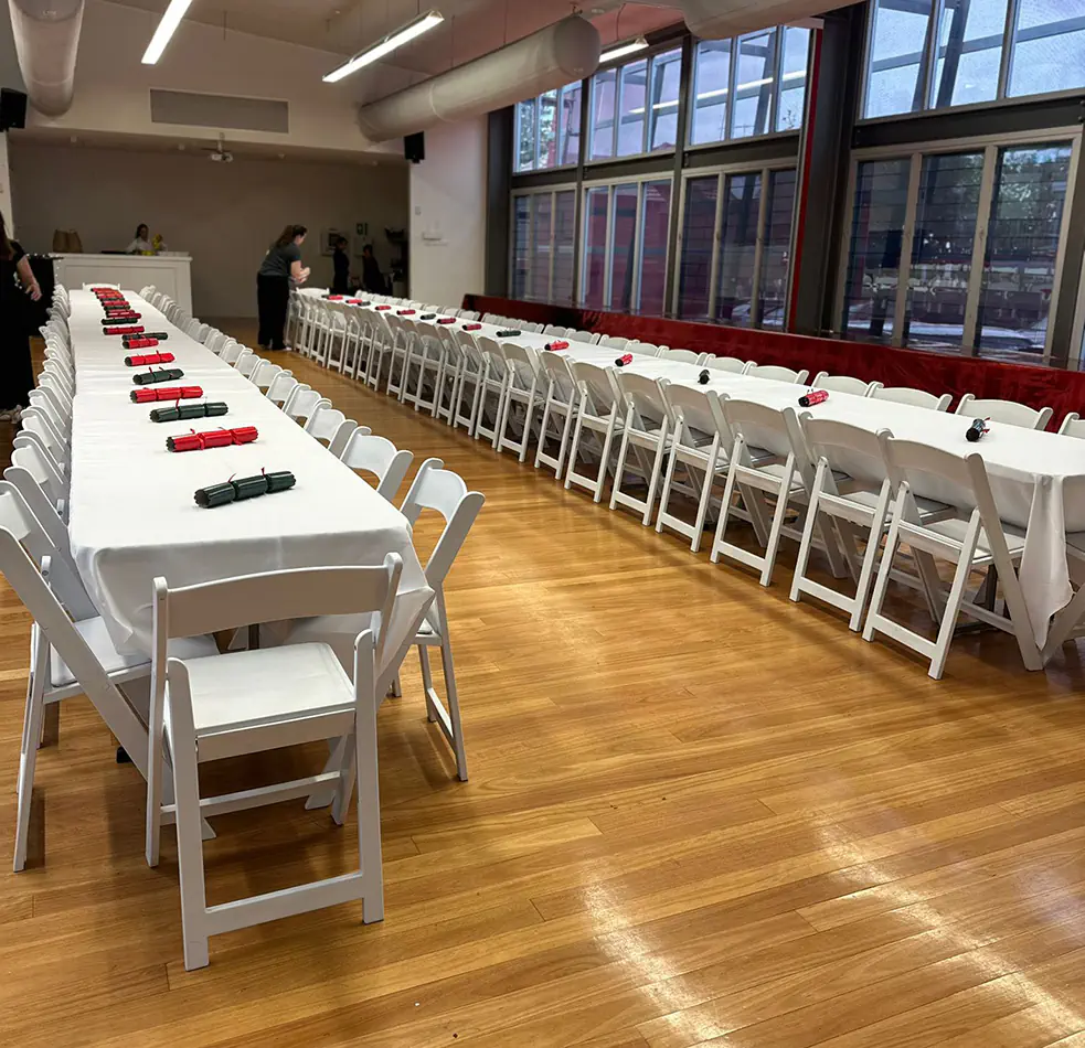 Long white banquet tables with white folding chairs arranged for a formal indoor event dining setup