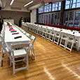 Long white banquet tables with white folding chairs arranged for a formal indoor event dining setup